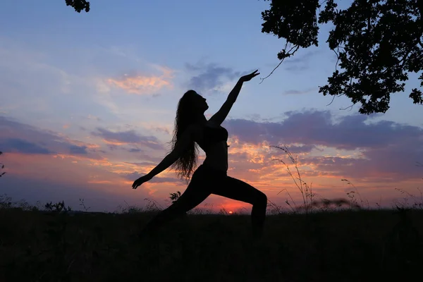 Une femme dans la nature en contre jour qui fait des positions de Yoga